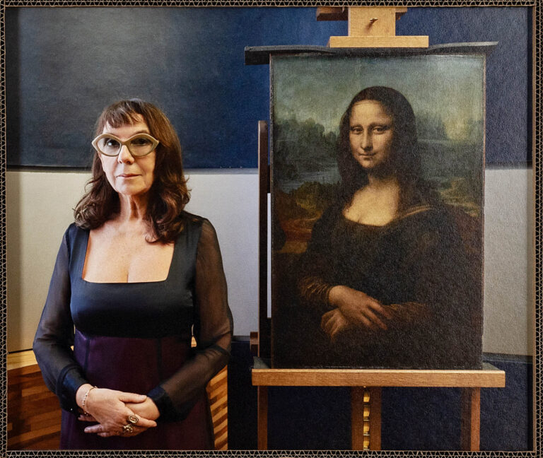 A color photograph depicts a woman in a black dress and glasses standing next to the Mona Lisa, Leonardo da Vinci’s famous painting of a woman.]